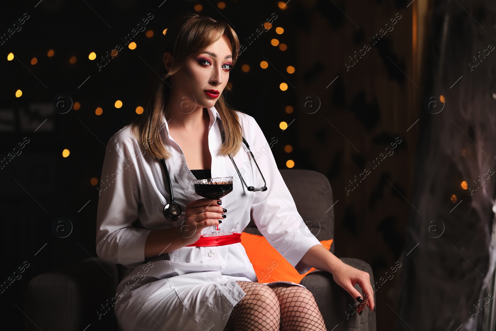 Photo of Woman in scary nurse costume with glass of wine against blurred lights indoors, space for text. Halloween celebration