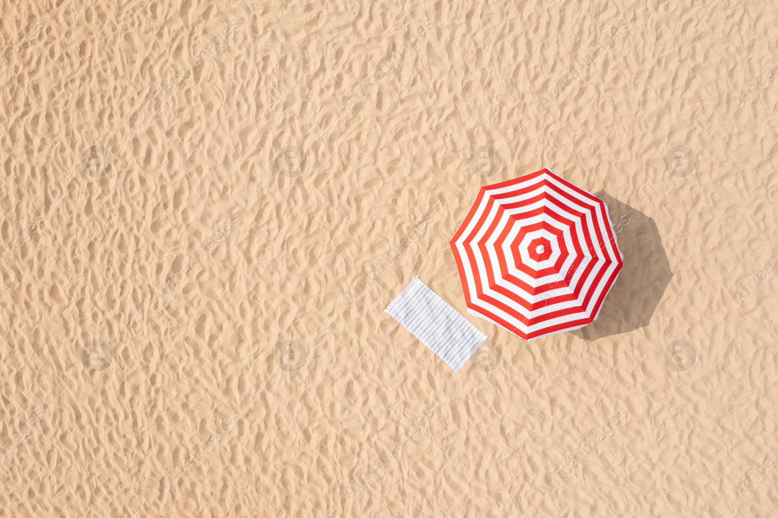 Image of Striped beach umbrella near towel on sand, aerial view. Space for text