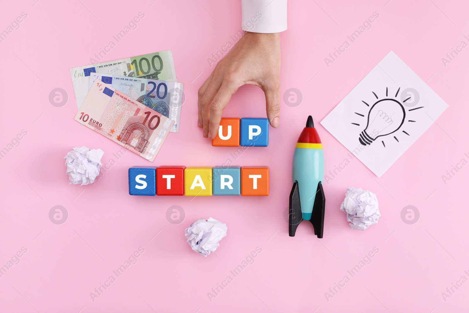 Photo of Woman forming words Start Up with colorful cubes on pink background, top view