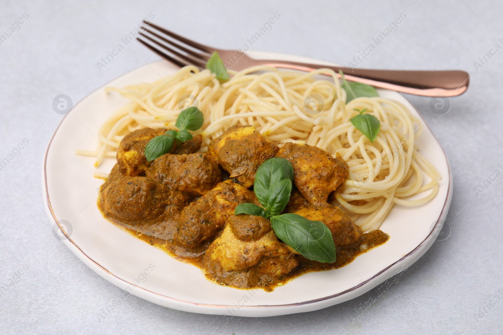 Photo of Delicious chicken, pasta with curry sauce and basil served on white table