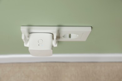 Photo of Wireless Wi-Fi repeater on light green wall indoors, above view