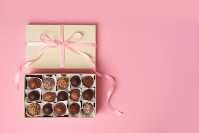 Photo of Box of delicious chocolate candies on pink background, top view. Space for text