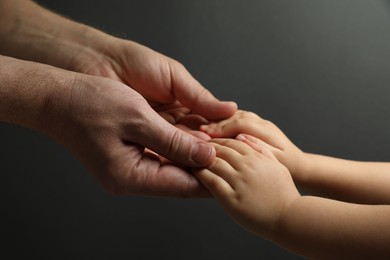 Photo of Father and child holding hands on dark grey background, closeup