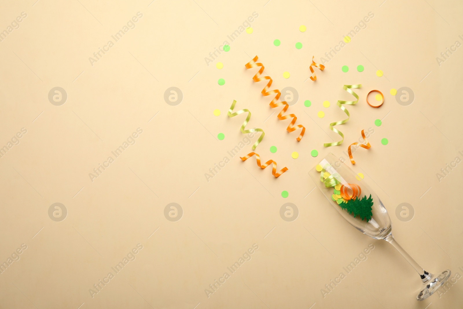 Photo of Glass and shiny confetti on beige background, flat lay. Space for text