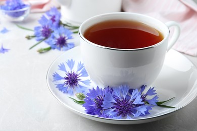 Photo of Cup of tea and cornflowers on light table, closeup
