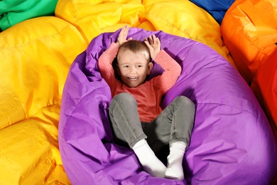Photo of Cute child playing on colorful bean bag chairs indoors