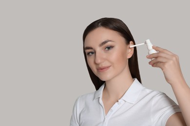 Young woman using ear spray on light grey background. Space for text