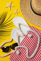 Photo of Flat lay composition with bag, palm leaf and other beach accessories on yellow background