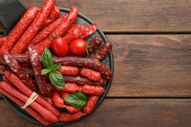 Different thin dry smoked sausages, basil and tomatoes on wooden table, top view. Space for text