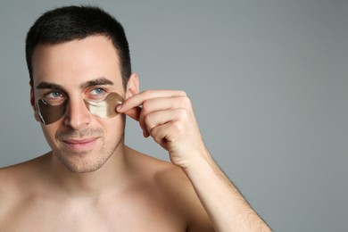 Young man applying under eye patches on grey background. Space for text