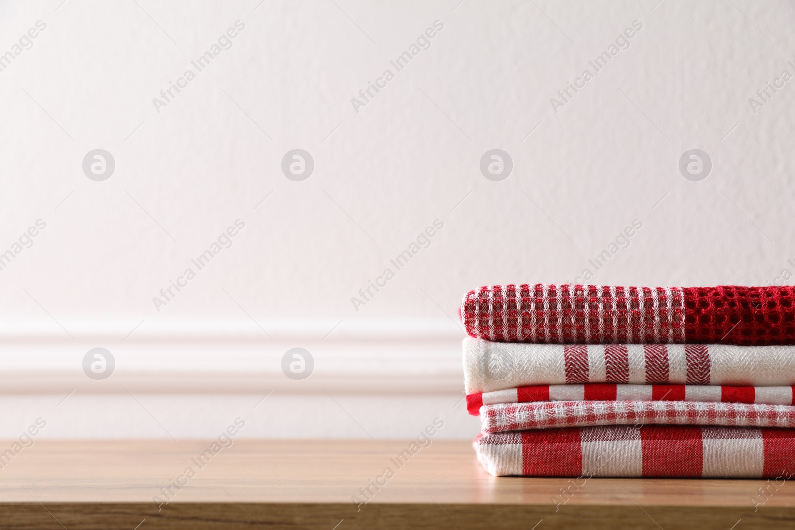Photo of Stack of kitchen towels on wooden table near white wall. Space for text