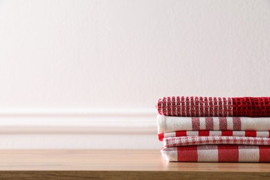 Stack of kitchen towels on wooden table near white wall. Space for text