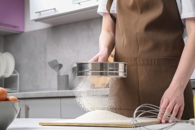 Photo of Woman sieving flour at table in kitchen, closeup