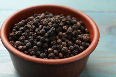 Photo of Aromatic spice. Black pepper in bowl on light blue wooden table, closeup