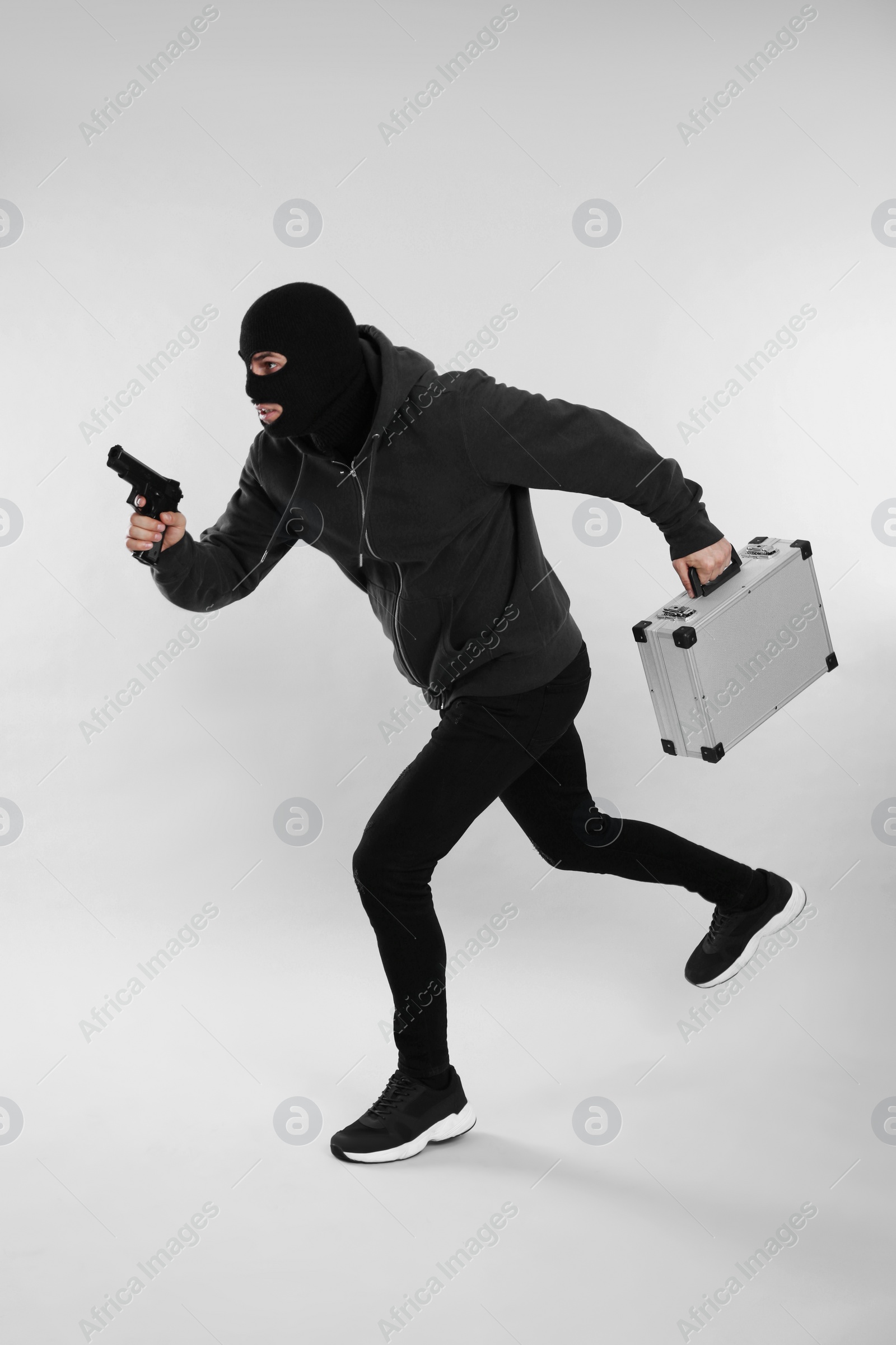 Photo of Man wearing black balaclava with metal briefcase and gun on light grey background