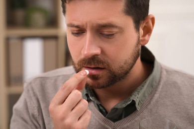 Photo of Depressed man taking antidepressant pill on blurred background, closeup