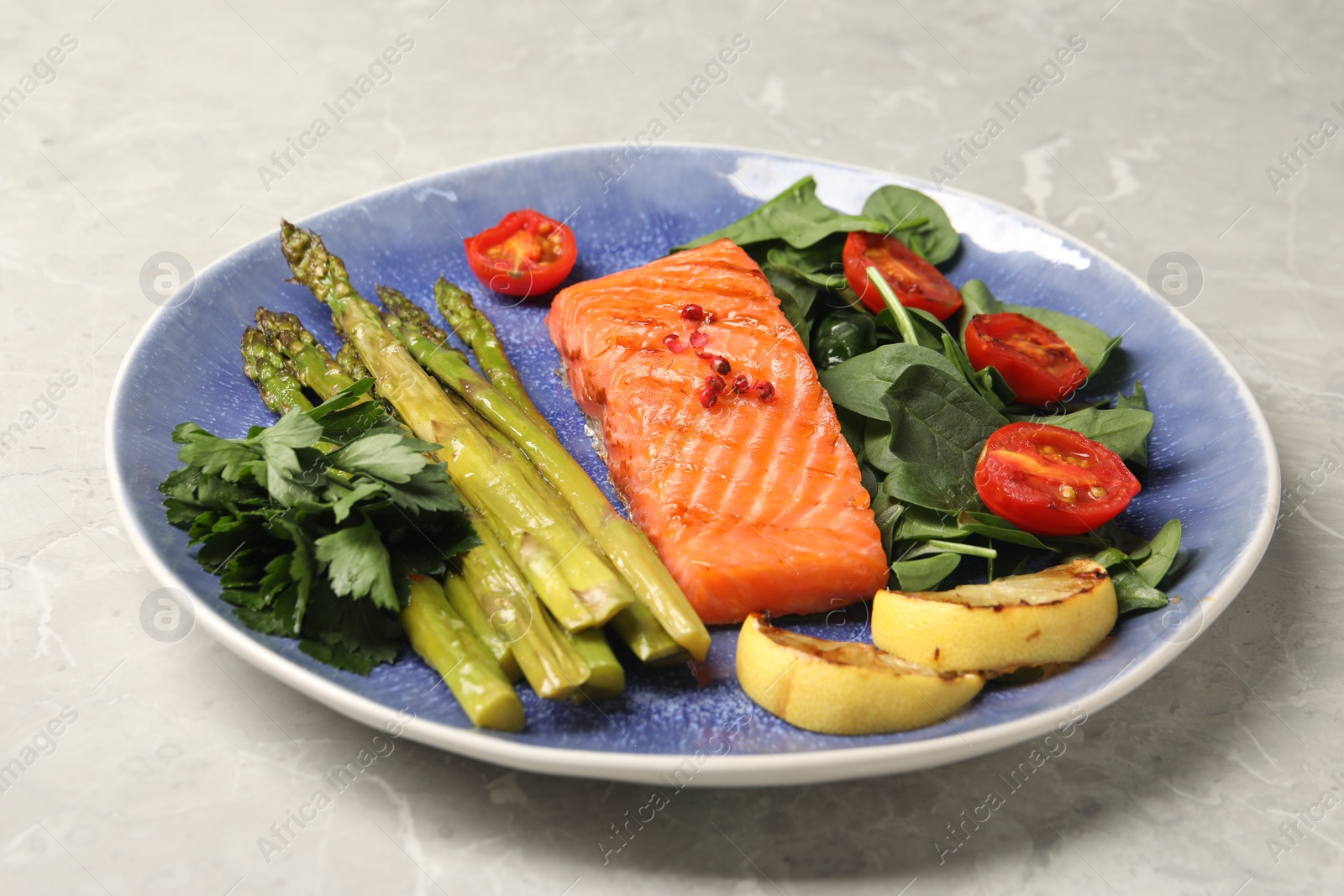 Photo of Tasty grilled salmon with tomatoes, asparagus, lemon and basil on grey table, closeup