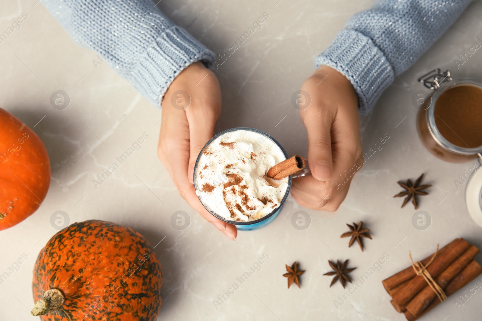 Photo of Woman holding glass cup with pumpkin spice latte and whipped cream on light background, top view