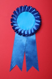 Photo of Blue award ribbon on red background, top view
