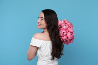 Photo of Beautiful young woman with bouquet of pink peonies against light blue background