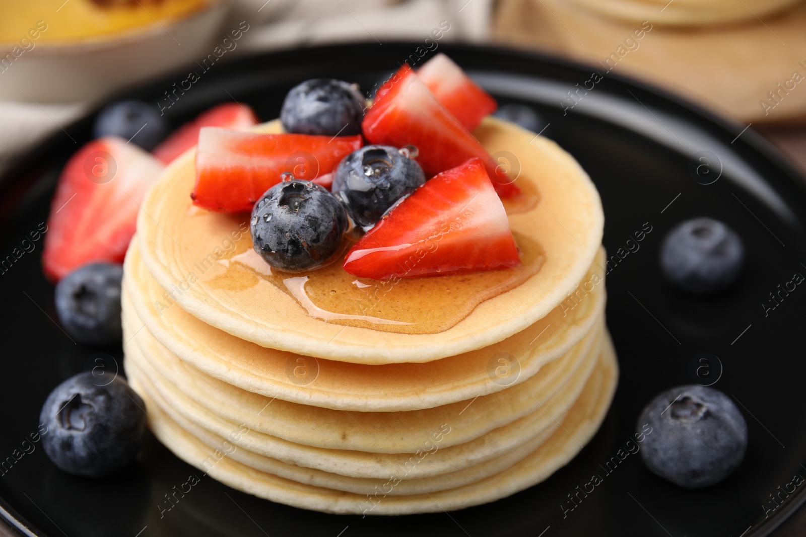 Photo of Delicious pancakes with strawberries and blueberries on black plate, closeup