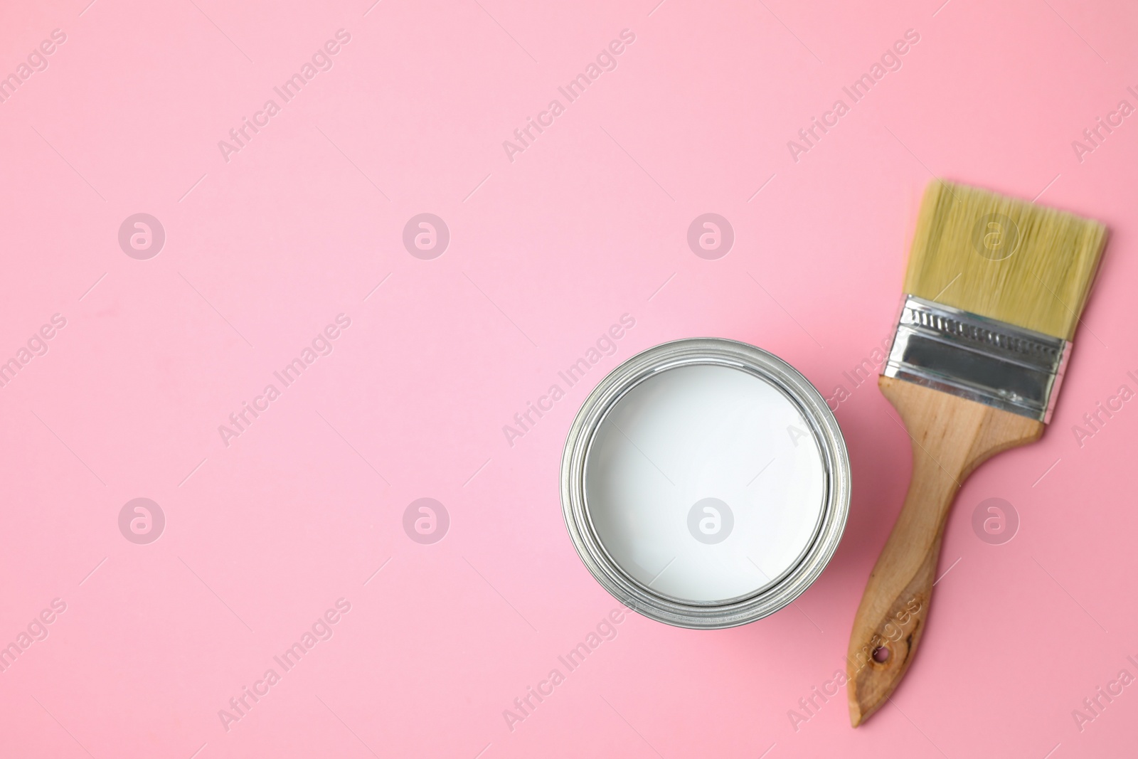 Photo of Open can with white paint and brush on pink background, flat lay. Space for text