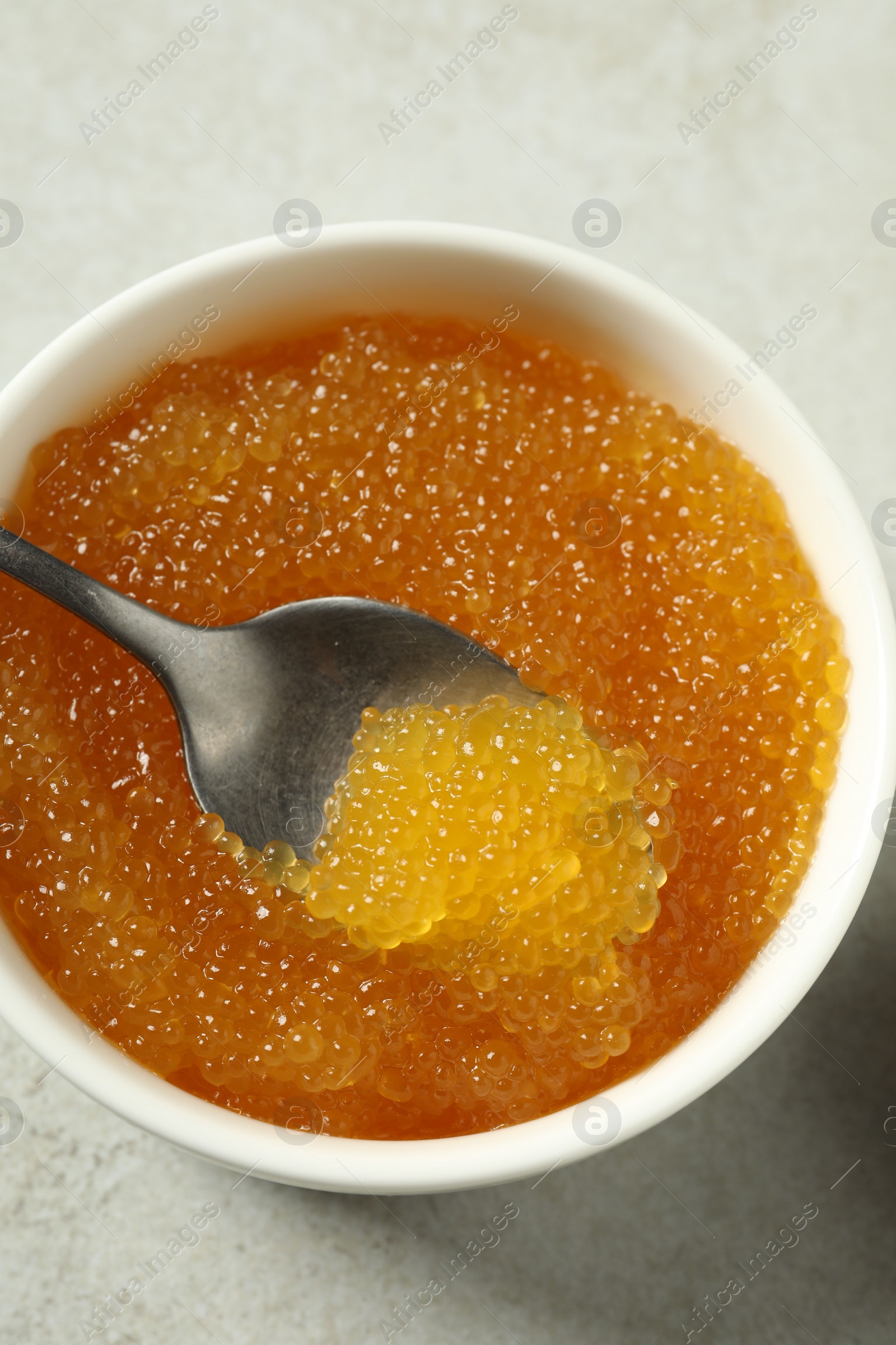 Photo of Fresh pike caviar in bowl and spoon on light grey table, top view