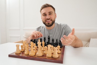 Photo of Happy young man playing chess at white table indoors