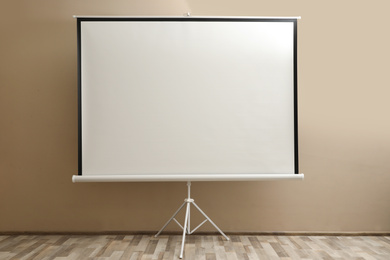 Photo of Blank projection screen near beige wall indoors. Space for design