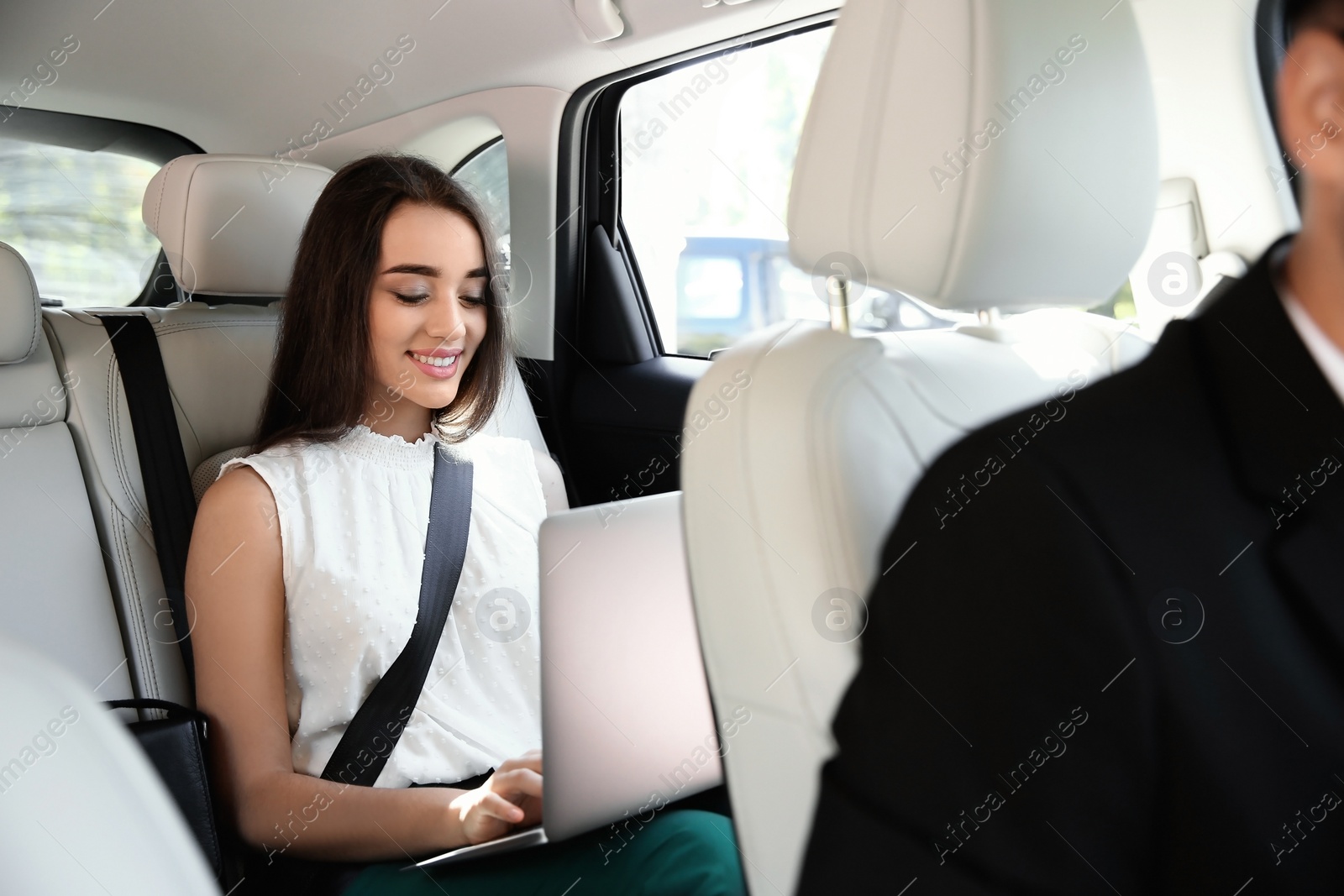 Photo of Young businesswoman with laptop and driver in luxury car. Chauffeur service