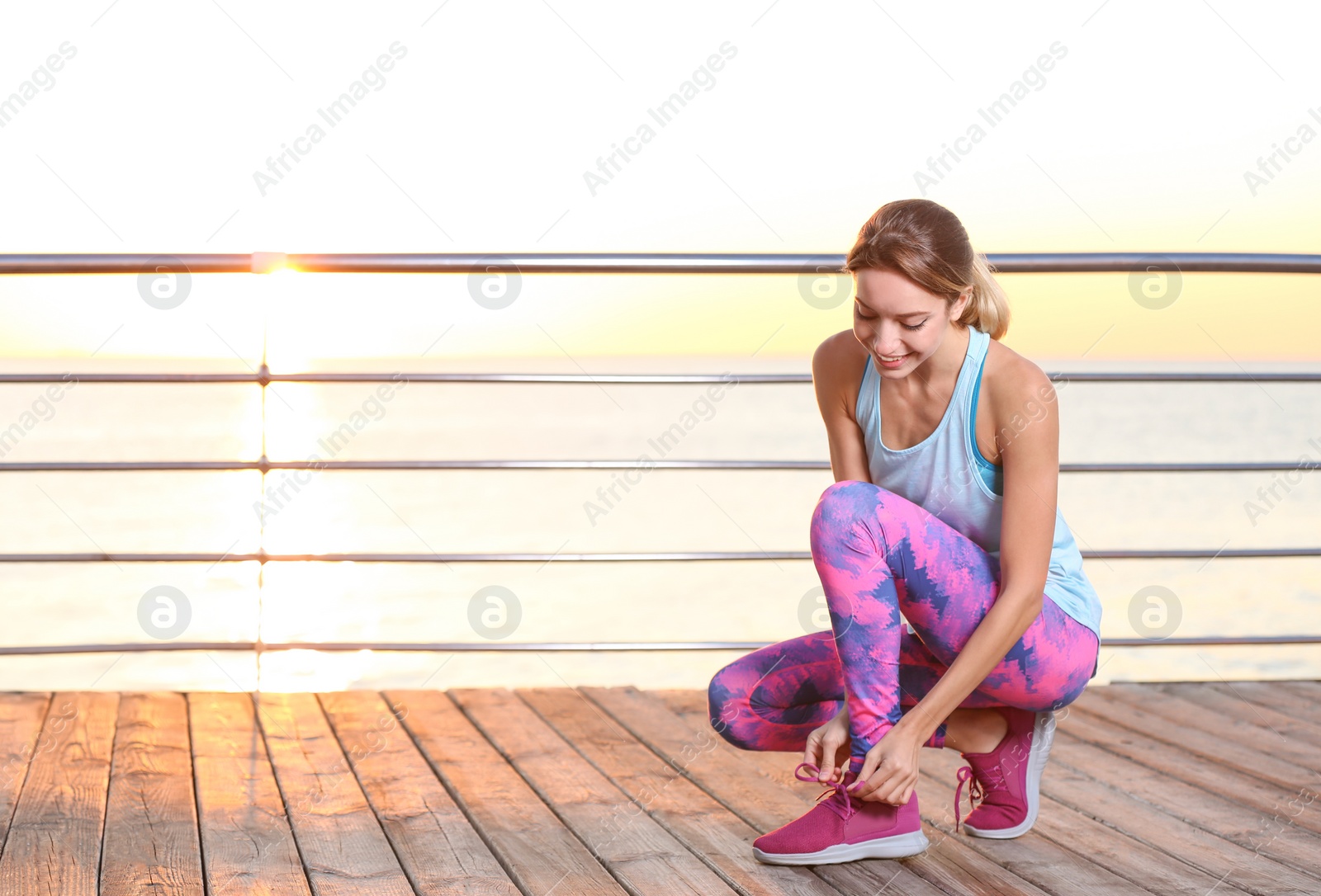 Photo of Young woman tying shoelaces on pier. Morning workout