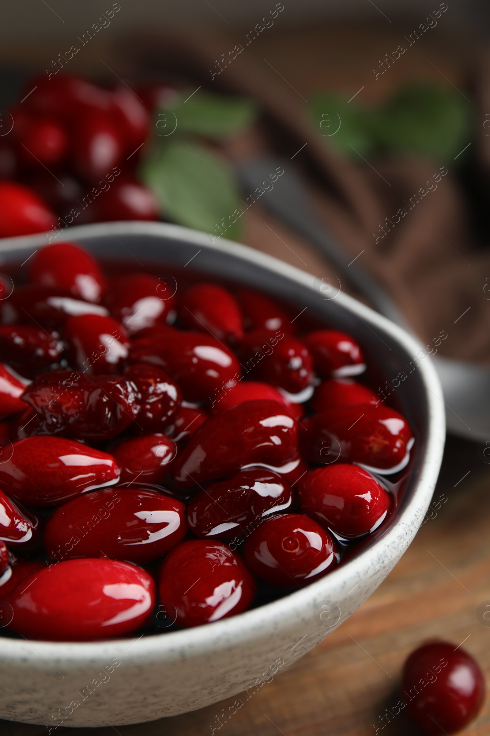 Photo of Delicious dogwood jam with berries in bowl on wooden table, closeup