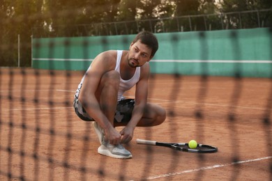 Photo of Handsome man tying shoelaces on tennis court