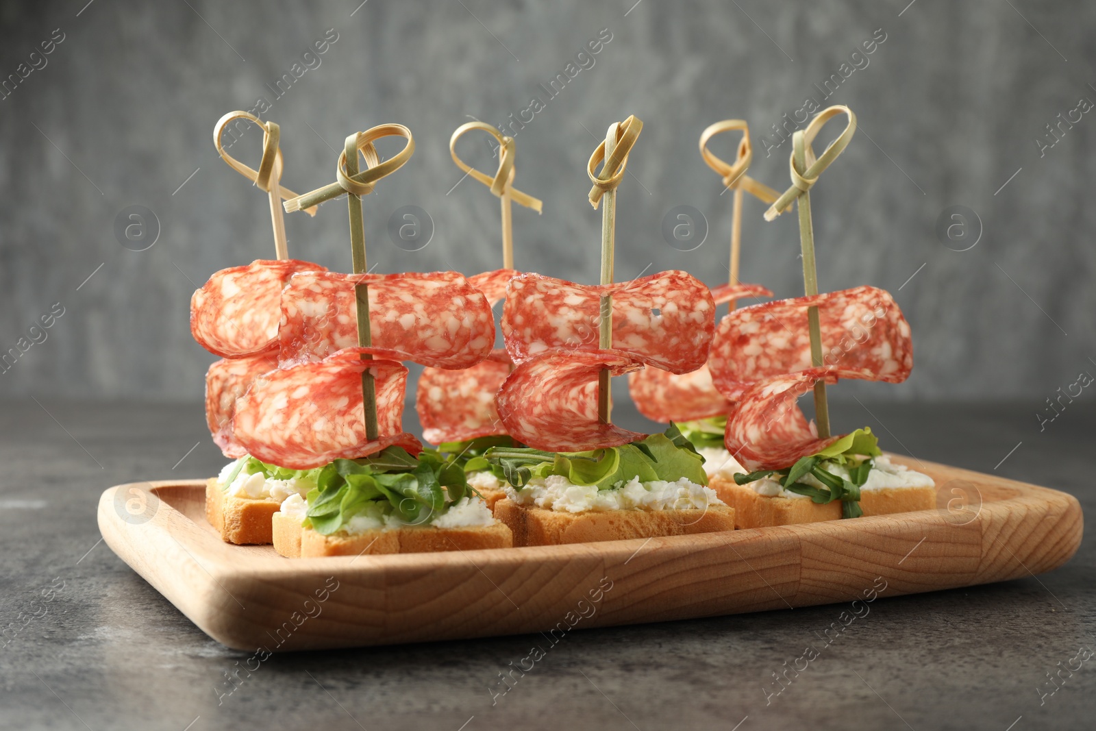 Photo of Tasty canapes with salami, greens and cream cheese on grey table