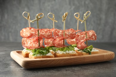 Photo of Tasty canapes with salami, greens and cream cheese on grey table