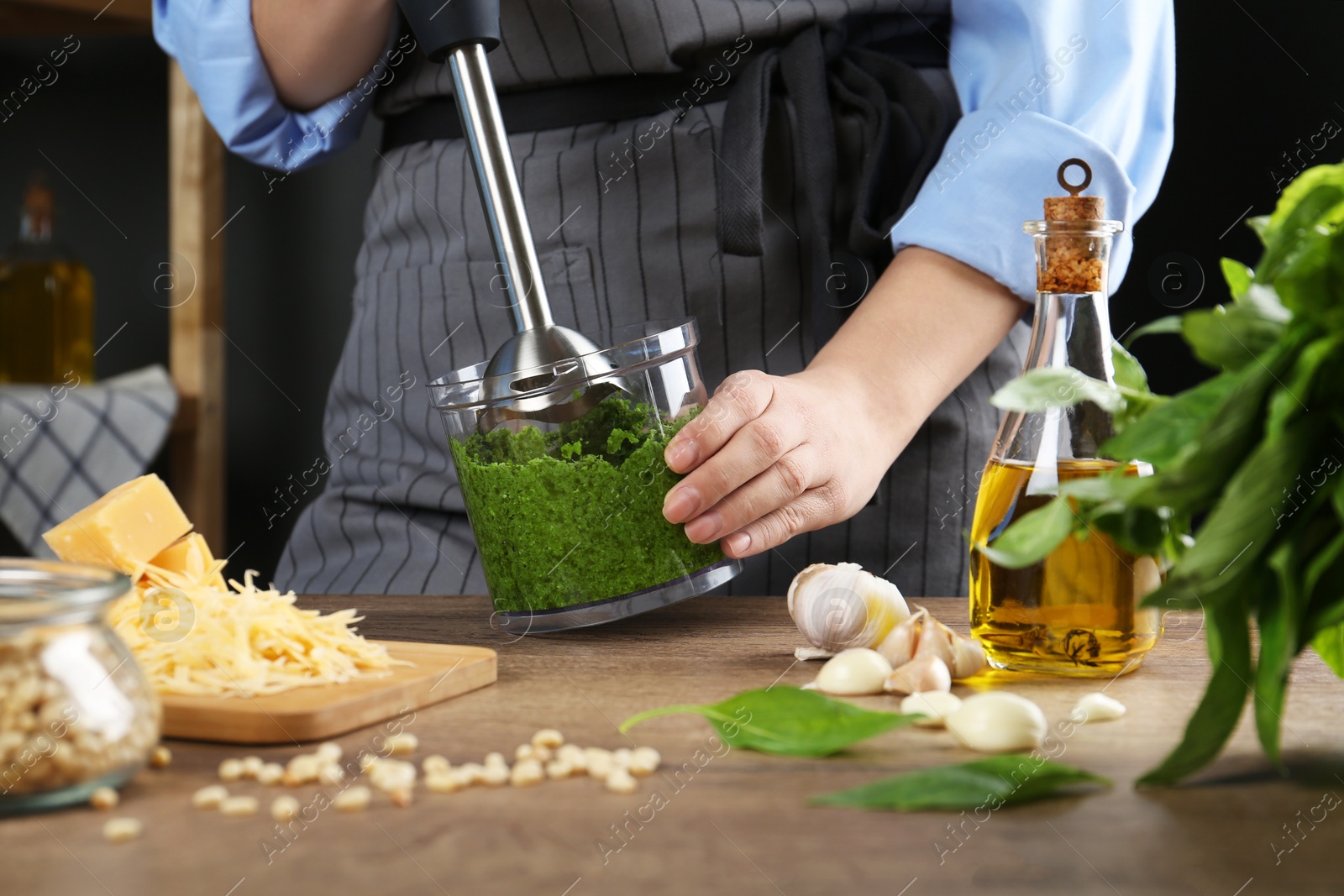 Photo of Woman blending pesto sauce in bowl at table, closeup