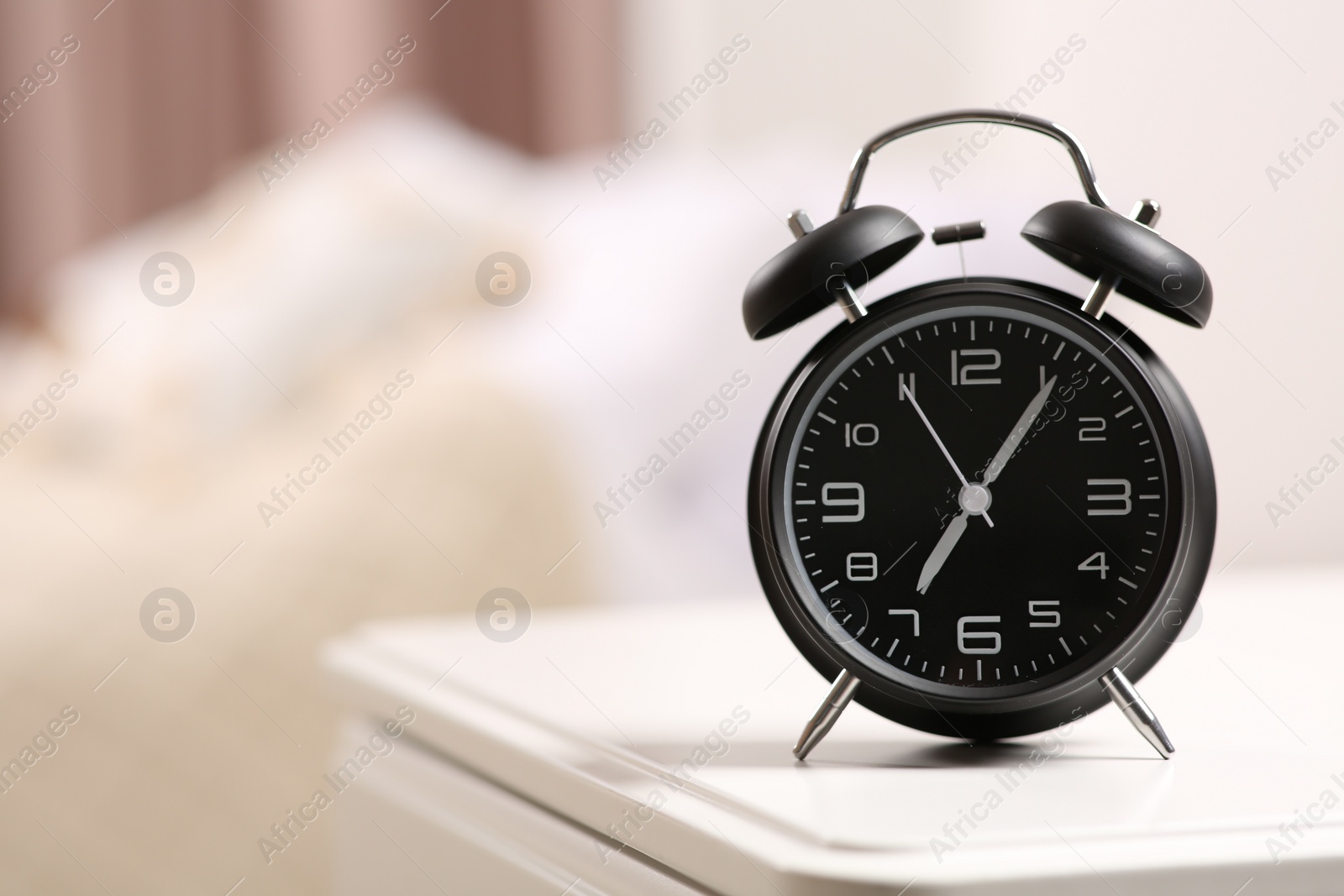 Photo of Black alarm clock on white nightstand indoors. Space for text