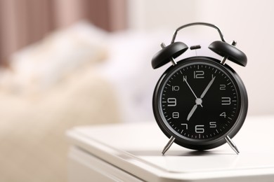 Black alarm clock on white nightstand indoors. Space for text