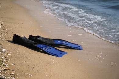 Pair of blue flippers on sand near sea. Space for text
