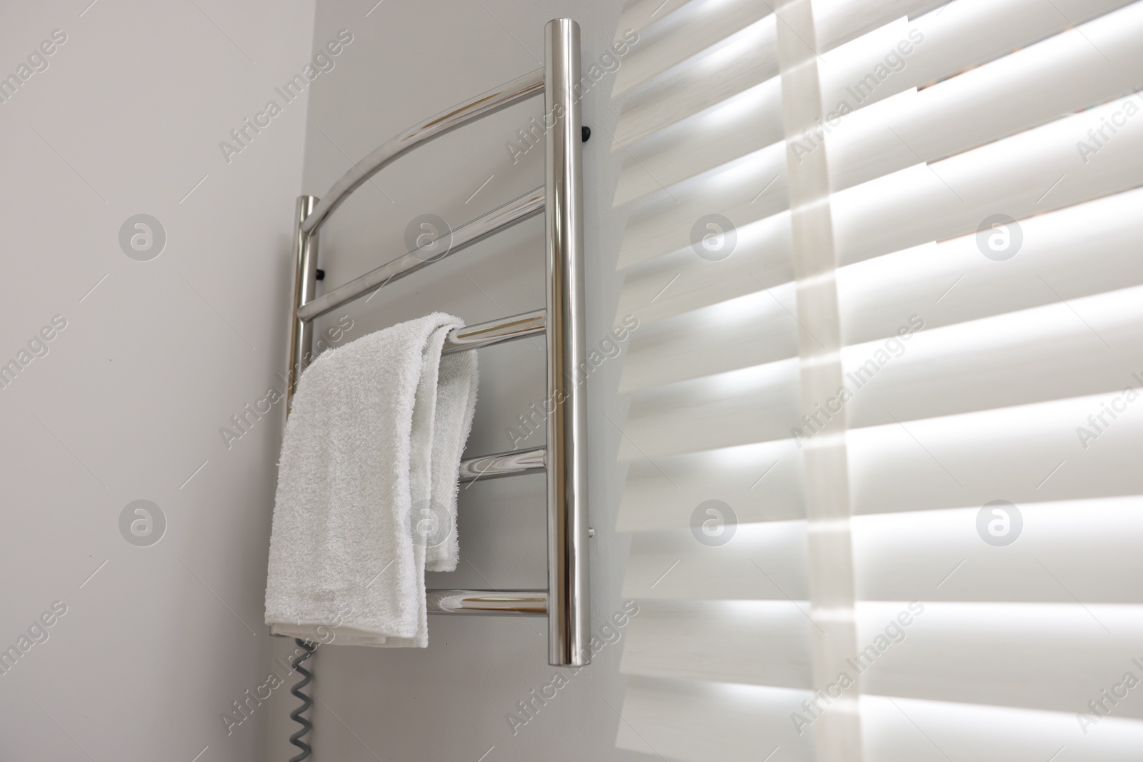 Photo of Heated rail with towel on white wall in bathroom, space for text