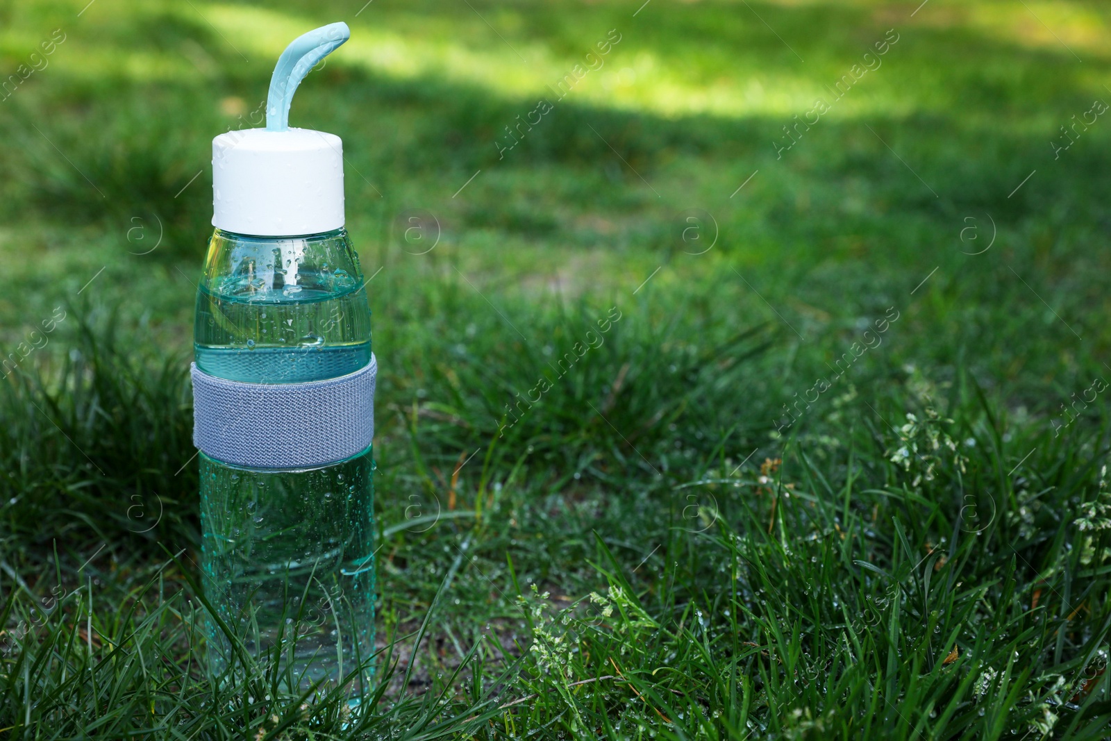 Photo of Glass bottle of fresh water on green grass outdoors. Space for text