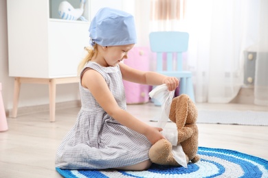 Photo of Cute child imagining herself as doctor while playing with toy bunny at home