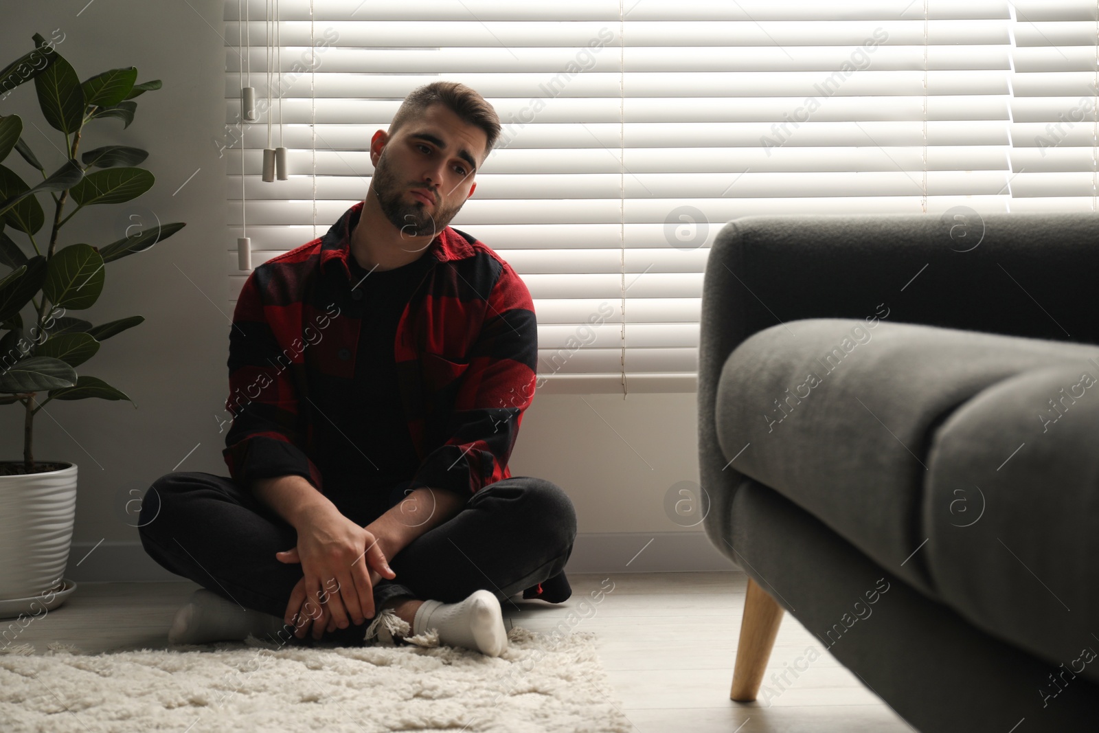 Photo of Sad man sitting near closed blinds indoors