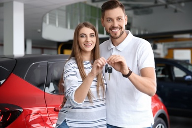 Photo of Happy woman and man with car keys in modern auto dealership