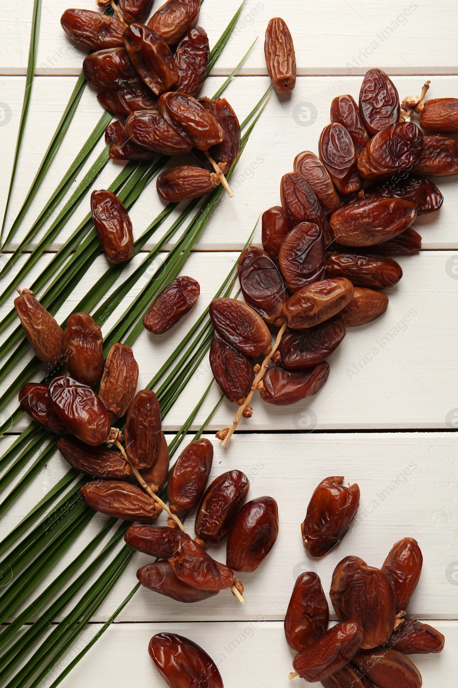 Photo of Sweet dried dates with palm leaf on white wooden table, flat lay