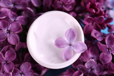 Jar of cream and beautiful lilac flowers as background, closeup