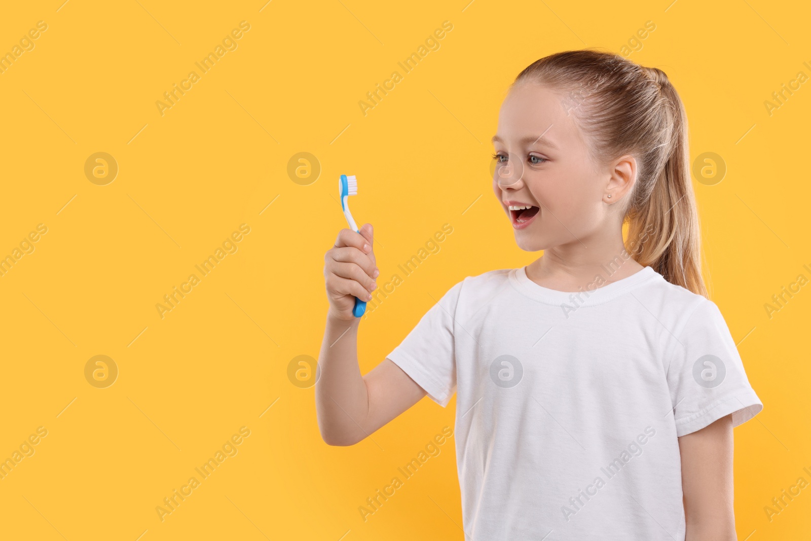 Photo of Happy girl holding toothbrush on yellow background. Space for text