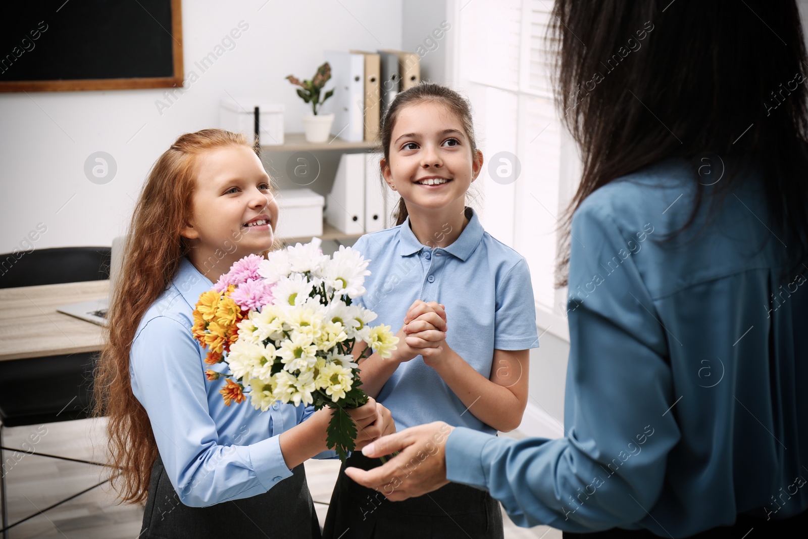 Photo of Schoolgirls congratulating their pedagogue with bouquet in classroom. Teacher's day