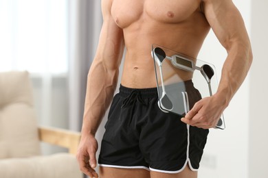 Photo of Athletic man holding scales at home, closeup. Weight loss concept
