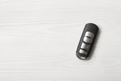 Remote car key on white wooden background, top view. Space for text